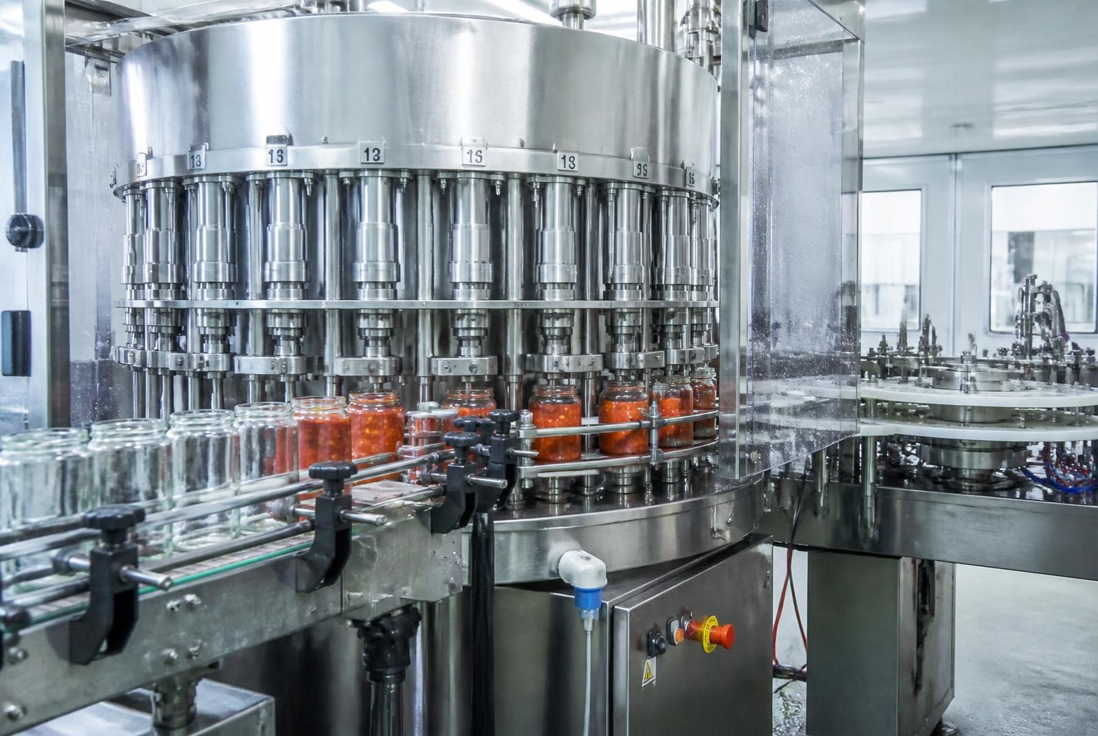 Rotary liquid filling machine dosing sauce into glass jars with conveyor, filling valves and safety guard