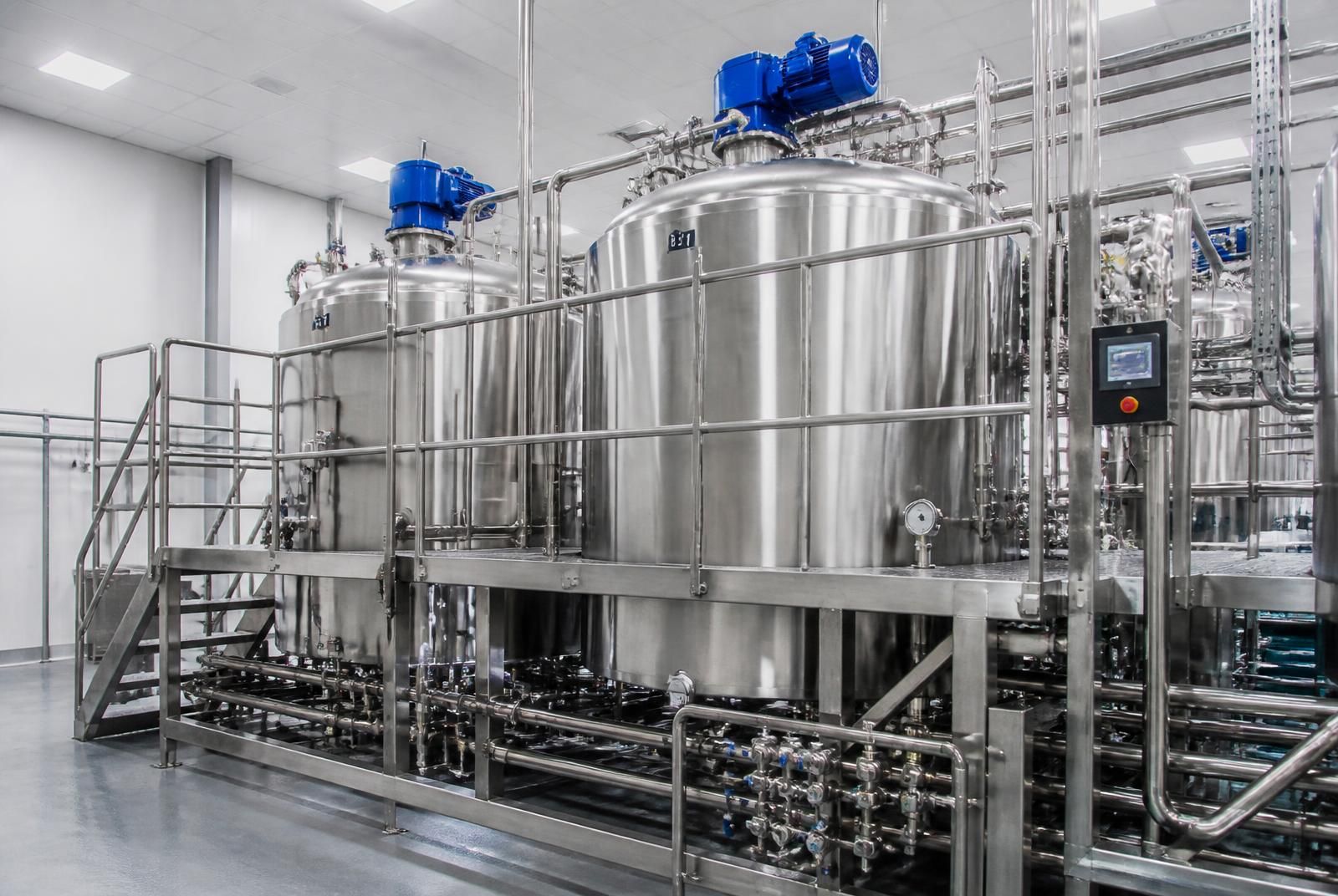 Stainless steel industrial mixing tanks with top-mounted agitator motors, valve manifold and operator platform in a food factory